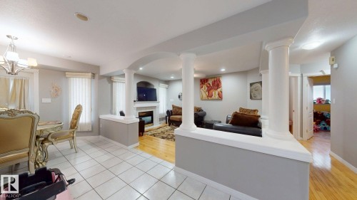 Spacious interior featuring a tiled dining area, a living area with wood-finish flooring, a decorative fireplace, and architectural columns defining the spaces - 3738 28A Street, Edmonton, AB 