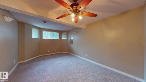 Carpeted interior space featuring a wood-finish ceiling fan with integrated lighting, a bay window with multiple panes, and neutral wall tones - 3738 28A Street, Edmonton, AB 