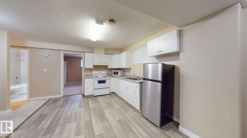 Kitchen area featuring wood-finish flooring, white cabinetry, a stainless steel refrigerator, and a white electric range - 3738 28A Street, Edmonton, AB 