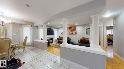 Open-concept room featuring white tile flooring, wood-finish flooring, a decorative fireplace, and architectural columns - 3738 28A Street, Edmonton, AB 