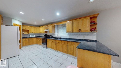 Kitchen featuring extensive wood-finish cabinetry with black hardware, dark speckled countertops, and a white tile backsplash - 3738 28A Street, Edmonton, AB 