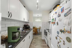 Galley kitchen featuring white cabinetry, black countertops, white subway tile backsplash, and wood-finish flooring - 