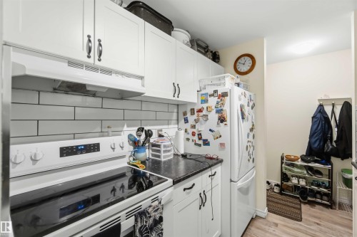 Kitchen featuring white cabinetry, dark countertops, white subway tile backsplash, and wood-finish flooring - 204 4601 131 Avenue, Edmonton, AB 