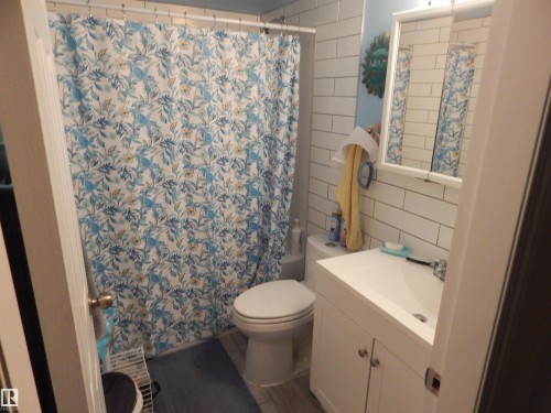 Bathroom featuring subway tile walls, a white vanity with integrated sink, a framed mirror, and wood-finish flooring - 204 4601 131 Avenue, Edmonton, AB 