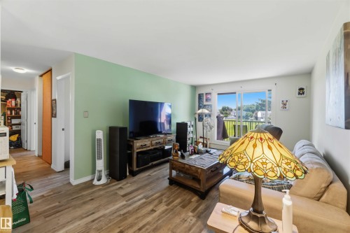 Open concept living area featuring wood-finish flooring, light green accent wall, and a sliding glass door to an outdoor space - 204 4601 131 Avenue, Edmonton, AB 