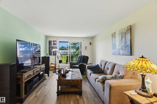 Living area featuring wood-finish flooring, a light green accent wall, and a sliding glass door providing outdoor access - 204 4601 131 Avenue, Edmonton, AB 