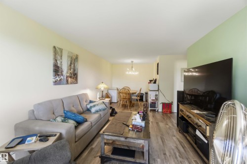 Open-concept living space featuring wood-finish flooring, a light-toned ceiling, and a dining area with a chandelier - 204 4601 131 Avenue, Edmonton, AB 