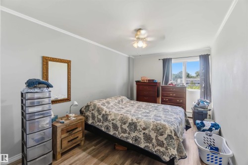 Spacious room featuring light gray walls, white crown molding, wood-finish flooring, a ceiling fan with integrated lighting, and a large window with white trim - 204 4601 131 Avenue, Edmonton, AB 