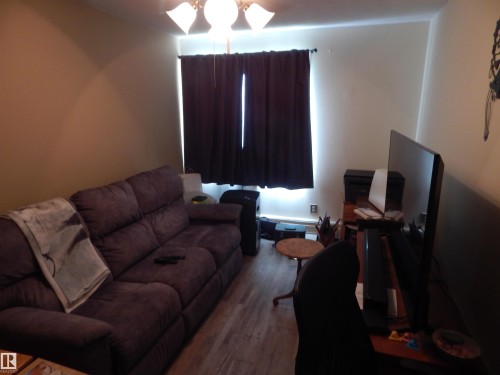 Wood-finish flooring throughout, featuring a window with dark drapery and a ceiling fan with integrated lighting - 204 4601 131 Avenue, Edmonton, AB 