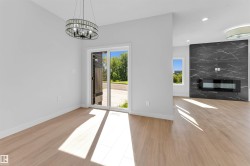 Open-concept living space with light wood-finish flooring, a modern electric fireplace with a dark marbled-effect tile surround, a contemporary chandelier, and a sliding glass door - 