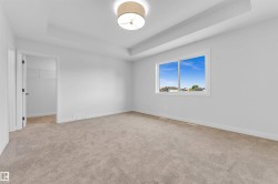 Spacious room featuring neutral carpeting, white walls, a tray ceiling, and a contemporary ceiling fixture - 