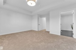 Spacious room with plush beige carpeting, recessed ceiling tray, and a contemporary ceiling light fixture - 
