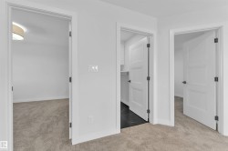 Hallway featuring plush light-colored carpeting, white interior doors with contemporary black hardware, and light-toned walls - 