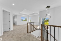 Upper level landing featuring light-colored carpet, a modern chandelier, and a wood and metal banister - 
