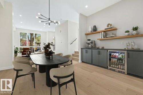 Dining area featuring wood-finish flooring, a contemporary chandelier, and a built-in beverage bar with floating wood shelves and a compact refrigerator - 10932 132 Street, Edmonton, AB - Indoor Photo Showing Dining Room