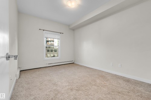 Carpeted room with a single window featuring blinds, a heating unit, and a ceiling-mounted light fixture - #209 10611 117 St Nw, Edmonton, AB - Indoor Photo Showing Other Room