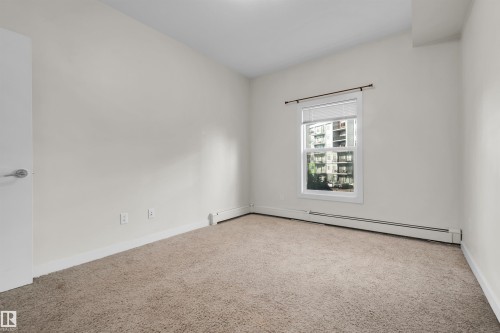 Neutral wall paint with baseboard trim, carpet flooring, single window with blinds, and a white door with a chrome handle - #209 10611 117 St Nw, Edmonton, AB - Indoor Photo Showing Other Room