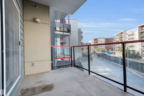 Private balcony featuring a concrete surface, glass railing with black posts and a red top rail, and a light fixture mounted on the exterior wall - #209 10611 117 St Nw, Edmonton, AB - Outdoor With Balcony With Exterior