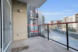 Private balcony featuring a concrete surface, glass railing with black posts and a red top rail, and a light fixture mounted on the exterior wall - 
