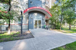 Contemporary building entrance featuring a curved red canopy, grey horizontal siding, and a glass-paneled entry door - 