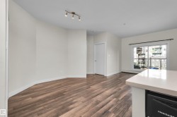 Open-concept living area with wood-finish flooring, track lighting, and a white interior door - 