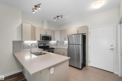 Kitchen featuring light-toned cabinetry and countertops, stainless steel appliances, a double basin sink, track lighting, and under-cabinet lighting - 