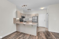 Contemporary kitchen featuring light wood-finish cabinetry, stainless steel appliances, and a breakfast bar with a neutral-toned countertop - 