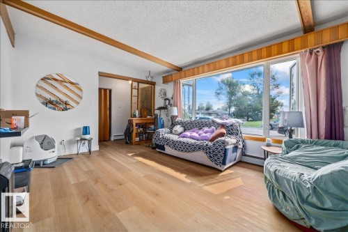 Living area with wood-finish flooring, exposed wooden ceiling beams, and a wide picture window - 8736 72 Street Nw, Edmonton, AB - Indoor Photo Showing Bedroom