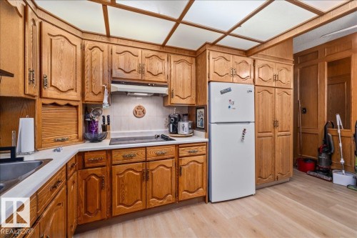 Kitchen featuring abundant wood cabinetry, an integrated cooktop, a white refrigerator, light-toned countertops, and wood-finish flooring - 8736 72 Street Nw, Edmonton, AB - Indoor Photo Showing Kitchen