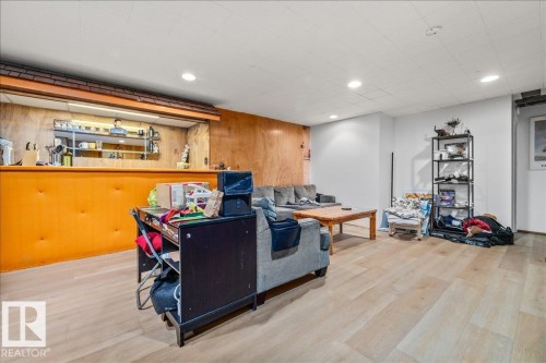 Wood-finish flooring throughout a spacious room featuring a built-in bar with wood paneling and shelving, recessed lighting, and white painted walls - 8736 72 Street Nw, Edmonton, AB - Indoor