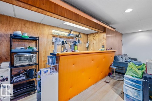 Recessed bar area featuring wood-paneled walls, an orange-upholstered bar counter, and overhead lighting - 8736 72 Street Nw, Edmonton, AB - Indoor