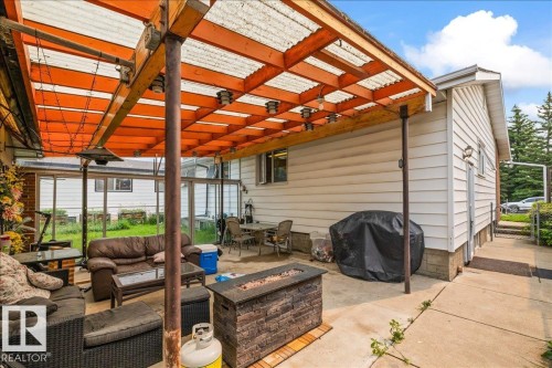 Expansive concrete patio area featuring a slatted wood-frame pergola with a corrugated translucent roof - 8736 72 Street Nw, Edmonton, AB - Outdoor With Deck Patio Veranda With Exterior