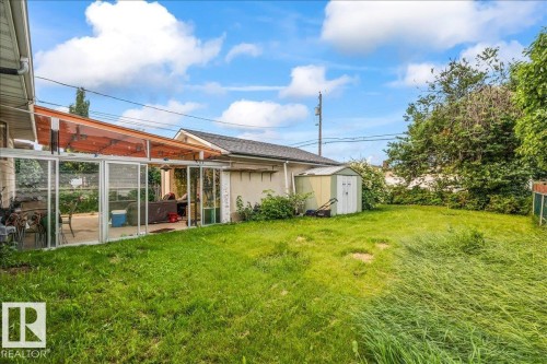 Rear yard with a glass-enclosed patio structure, an adjacent storage shed, and mature perimeter trees - 8736 72 Street Nw, Edmonton, AB - Outdoor