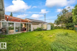 Rear yard with a glass-enclosed patio structure, an adjacent storage shed, and mature perimeter trees - 