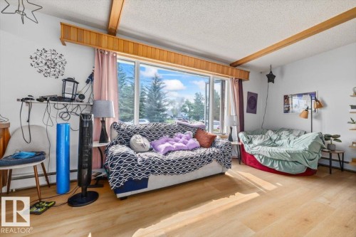 Bright living area featuring expansive windows, wood-finish flooring, exposed ceiling beams, and white walls - 8736 72 Street Nw, Edmonton, AB - Indoor Photo Showing Bedroom