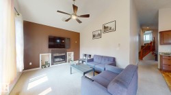 Vaulted ceiling living area featuring a ceiling fan, fireplace with dark tile surround, built-in shelving, and light-toned carpeting - 