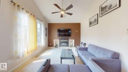 Vaulted ceiling living area featuring a built-in electric fireplace with stone surround, a ceiling fan, and carpet flooring - 