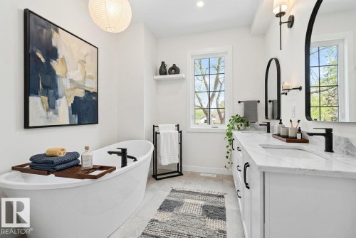 Contemporary bathroom featuring a freestanding soaking tub with a matte black faucet, a dual vanity with white cabinetry and stone countertops, and two arched mirrors - 10934 132 Street, Edmonton, AB - Indoor Photo Showing Bathroom