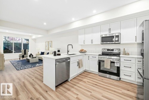 Bright kitchen featuring white cabinetry, stainless steel appliances, a white tile backsplash, and light wood-finish flooring - 10934 132 Street, Edmonton, AB - Indoor Photo Showing Kitchen