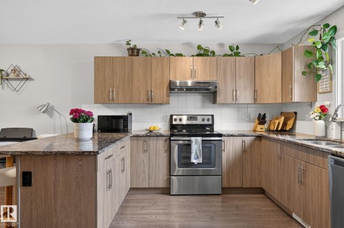 Modern kitchen featuring wood-finish cabinetry, speckled countertops, and stainless steel appliances - 33 Durrand Bend, Fort Saskatchewan, AB 