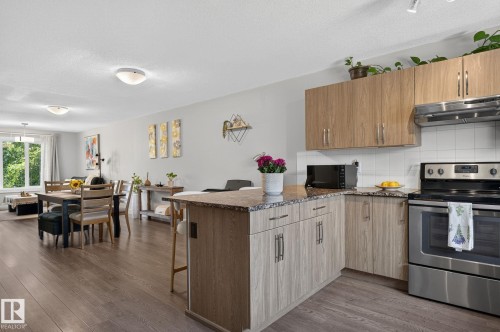 Open-concept living area featuring wood-finish flooring, a kitchen island with stone-finish countertop, and light-toned cabinetry - 33 Durrand Bend, Fort Saskatchewan, AB 