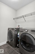 Laundry area featuring dark tile flooring, white baseboards, and a wire shelving unit - 