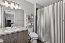 Bathroom featuring a wood-finish vanity with an integrated sink, a neutral countertop, and a contemporary light fixture - 