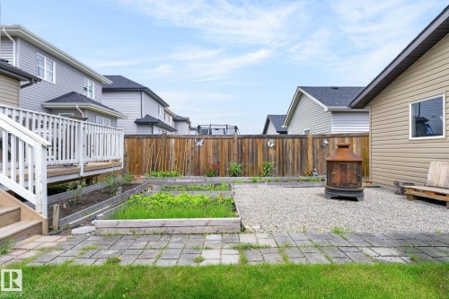 Fenced backyard featuring a gravel patio, raised garden beds, a wooden deck with railing, and a paver stone pathway - 33 Durrand Bend, Fort Saskatchewan, AB 