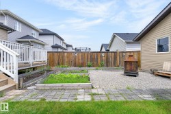 Fenced backyard featuring a gravel patio, raised garden beds, a wooden deck with railing, and a paver stone pathway - 
