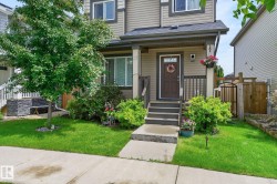 Inviting front entrance featuring a covered porch, wood-look siding, mature landscaping, and a concrete walkway - 