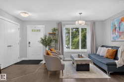 Open-concept living area featuring wood-finish flooring, a contemporary pendant light fixture, and a large multi-pane window - 