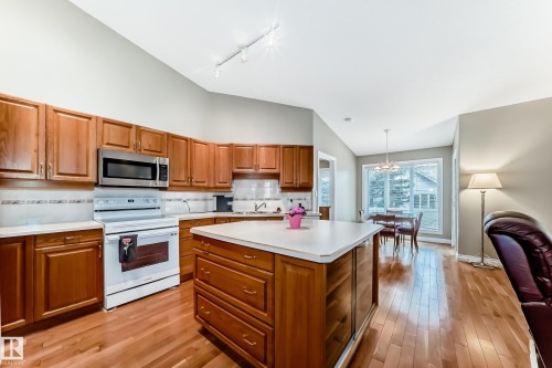 Kitchen featuring wood cabinetry, stainless steel microwave, white electric range, and a central island with integrated shelving - 29 929 Picard Drive, Edmonton, AB - Indoor Photo Showing Kitchen