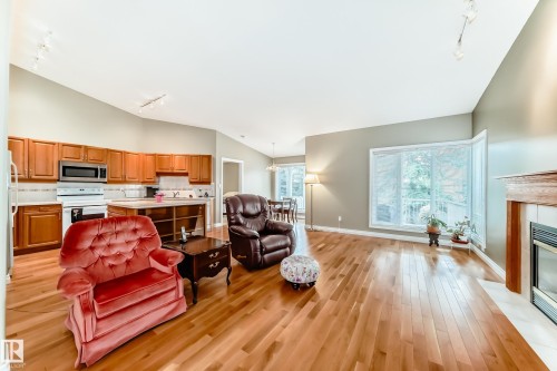 Open-concept living space with wood-finish flooring, a kitchen featuring wood cabinetry and stainless steel appliances, a bay window, and a fireplace with a wood mantel - 29 929 Picard Drive, Edmonton, AB - Indoor With Fireplace