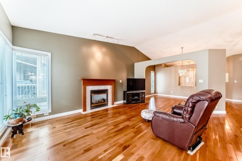Living area featuring wood-finish flooring, a fireplace with a wood mantel, vaulted ceilings, and large windows with horizontal blinds - 29 929 Picard Drive, Edmonton, AB - Indoor Photo Showing Living Room With Fireplace